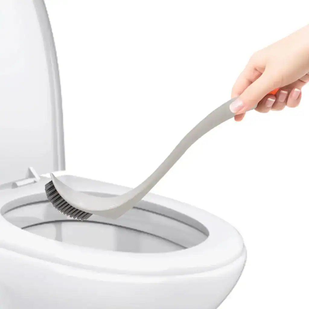Brosse WC incurvée en gris, utilisée pour nettoyer le WC avec une main.