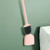 Brosse WC rose avec poignée longue, fixée sur un support mural près d'un WC.
