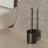 Brosse WC de qualité en noir, design moderne, posée dans un porte-brosse près d'un WC.