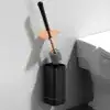 Brosse WC suspendue design avec poignée noire et tête brosse grise, fixée sur mur près de toilette.