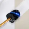 Brosse WC dorée avec poignée métallique et tête noire, dans un WC blanc, éclaboussure d'eau.
