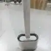 Brosse toilette flexible blanche avec poignée longue, emballée dans un film plastique transparent.