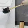 Brosse WC or avec manche doré et poils noirs, utilisée pour nettoyer le WC.
