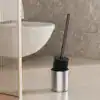 Brosse WC de qualité noire dans un porte-brosse en métal, près d'un WC moderne.